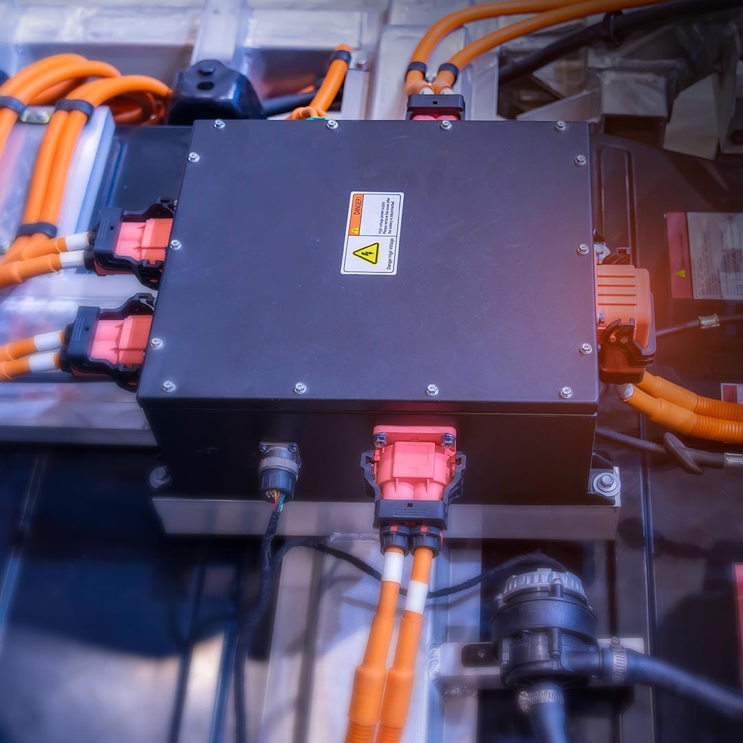 Electrical control box with orange cables, warning label, and connectors, part of an EV or high-voltage electrical system.