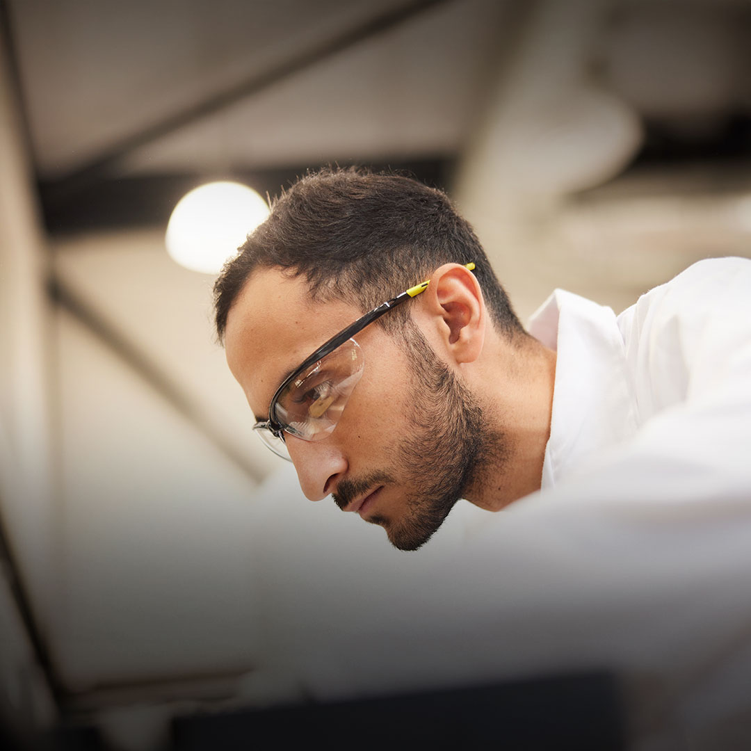 Man in safety glasses and white lab coat focuses on a scientific experiment in a laboratory.