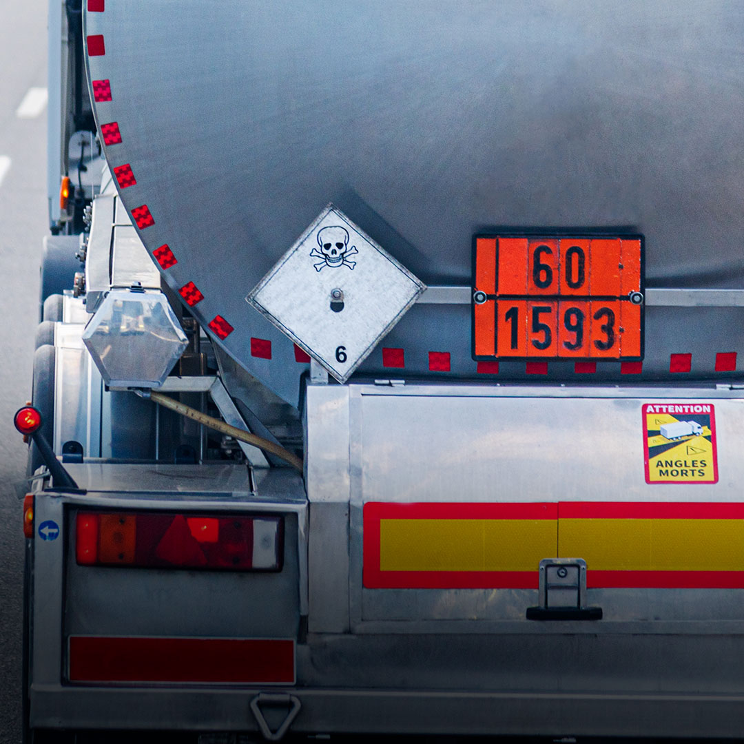 Back of tanker truck with hazardous materials sign, skull and crossbones, orange ID numbers, and blind spot warning sticker.