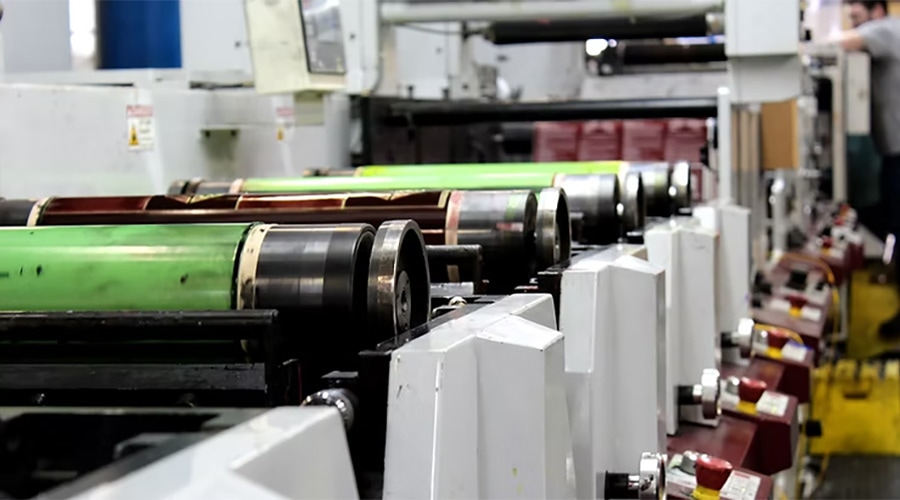 Close-up of industrial printing press with moving rollers and machinery processing paper in a factory environment.