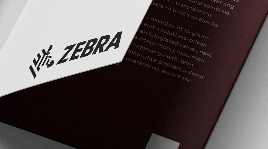 Folded white paper with bold black ZEBRA text and zebra head logo rests on maroon booklet with faded white marketing text.