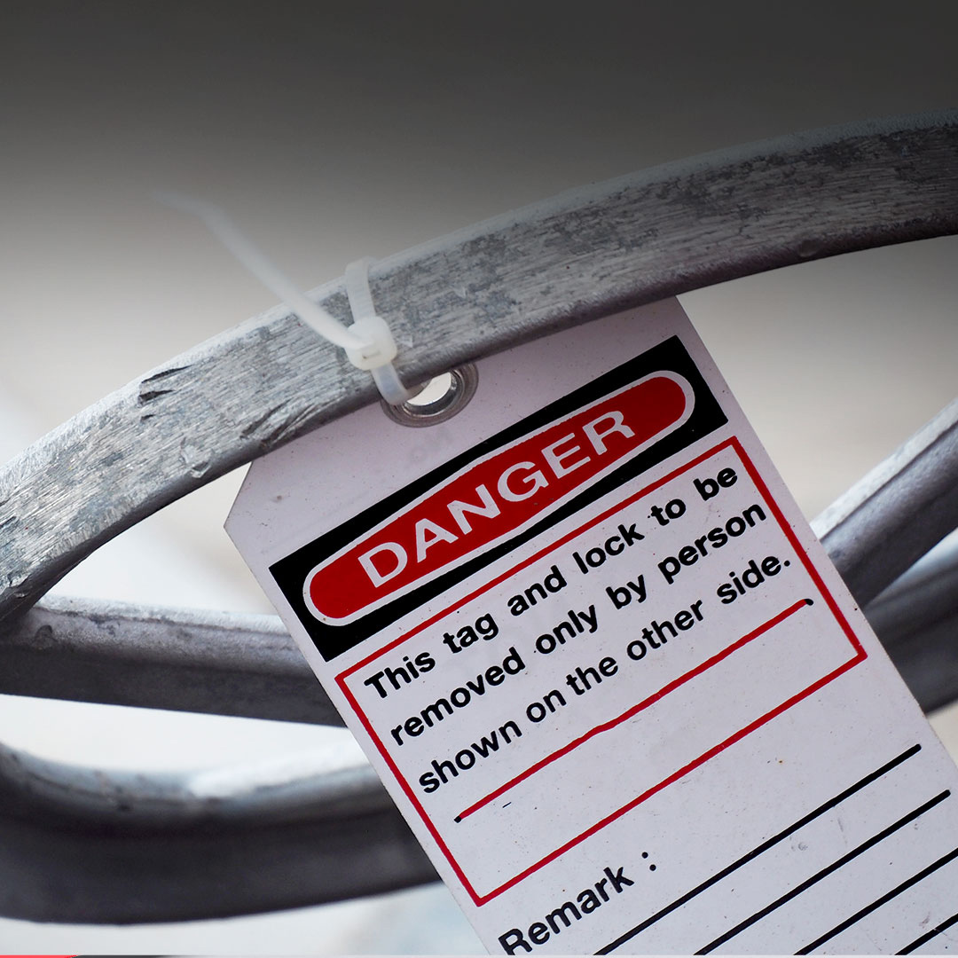 Close-up of a red Danger tag on a metal object with zip tie, stating only the named person may remove it; space for remarks at bottom.