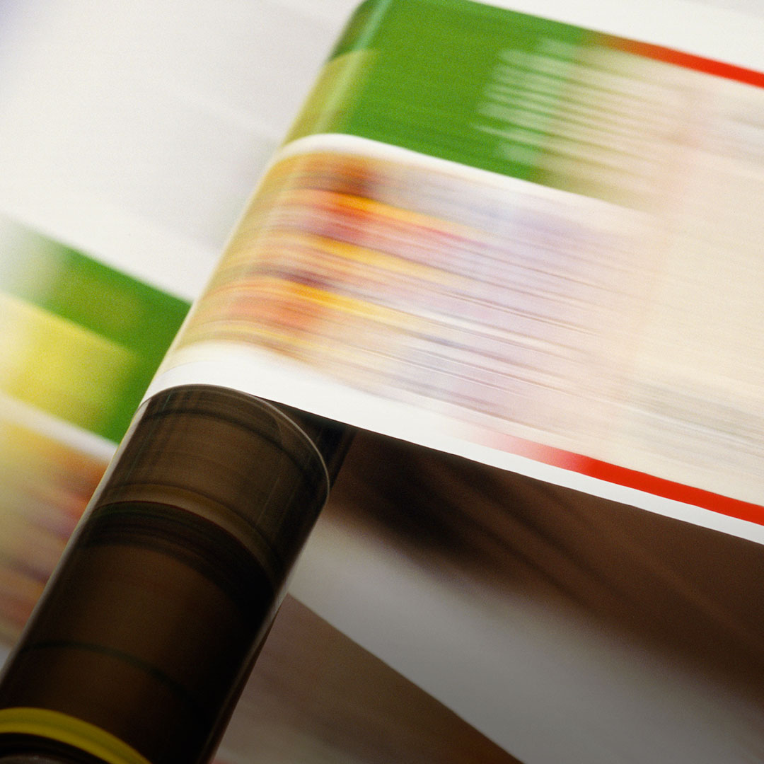 Close-up of a printing press running, colorful paper moving over a roller with green, red, and yellow motion blur.