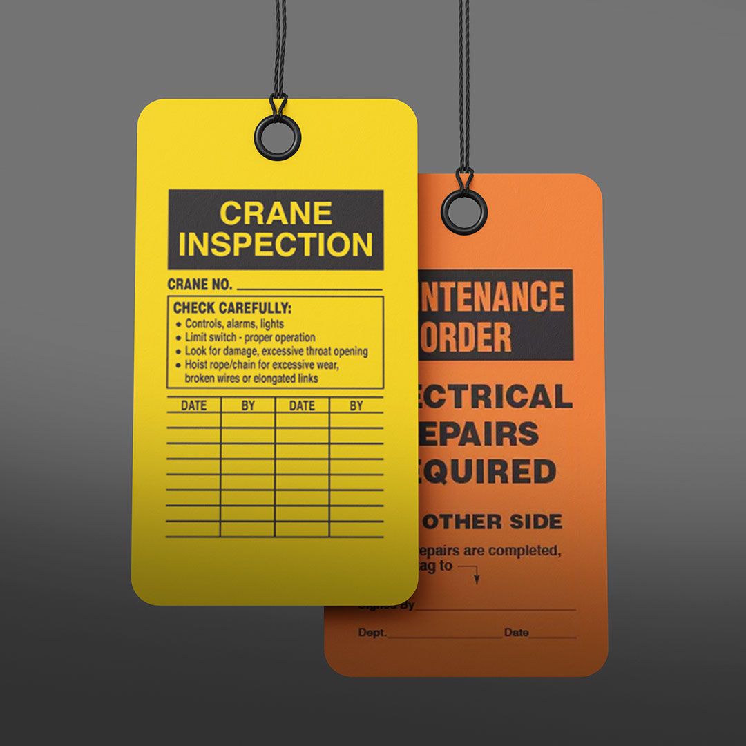 Yellow crane inspection tag with checklist and orange maintenance order tag for electrical repairs, both hanging by black strings.