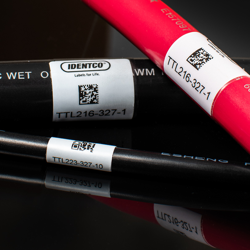 Red cable and two black cables with white barcode labels TTL216-327-1, TTL233-327-10, and IDENTCO Labels for Life on black surface.
