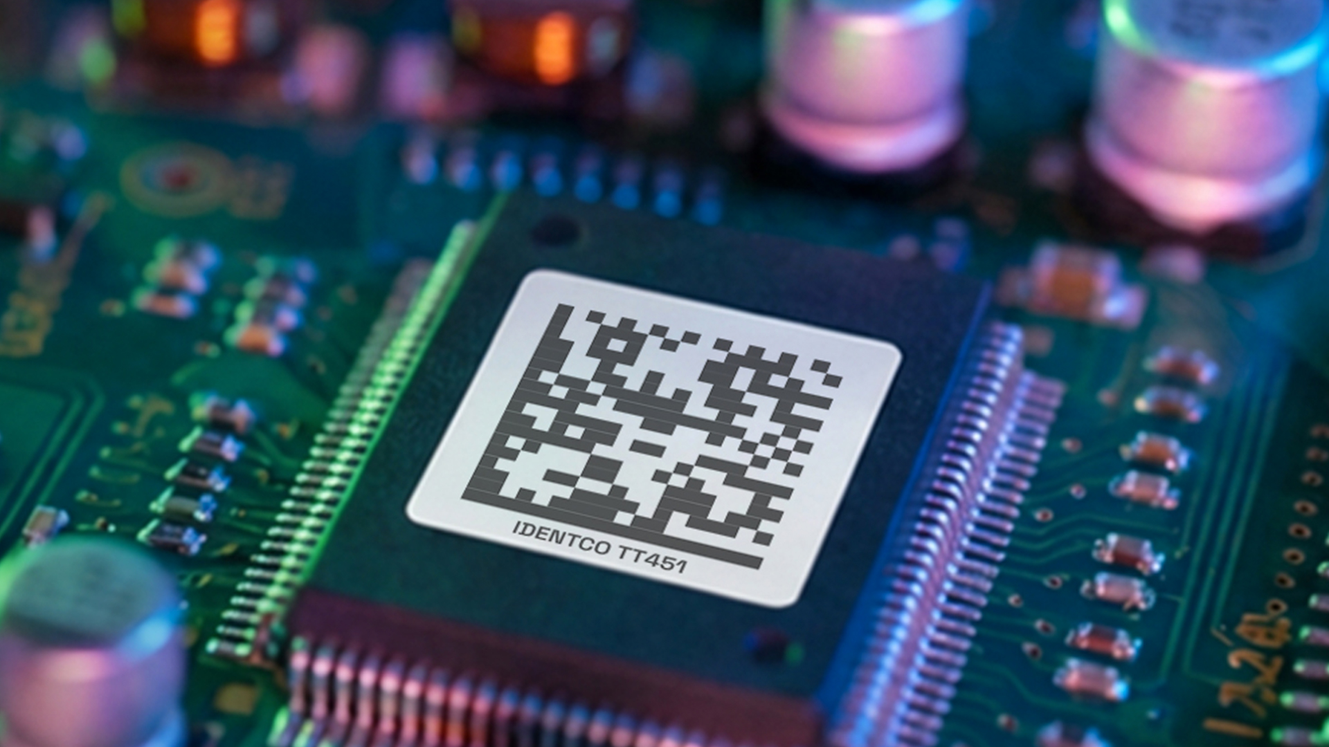 Close-up of a computer chip on a circuit board with QR code and IDENTCO TTA51 text visible on the chip surface.