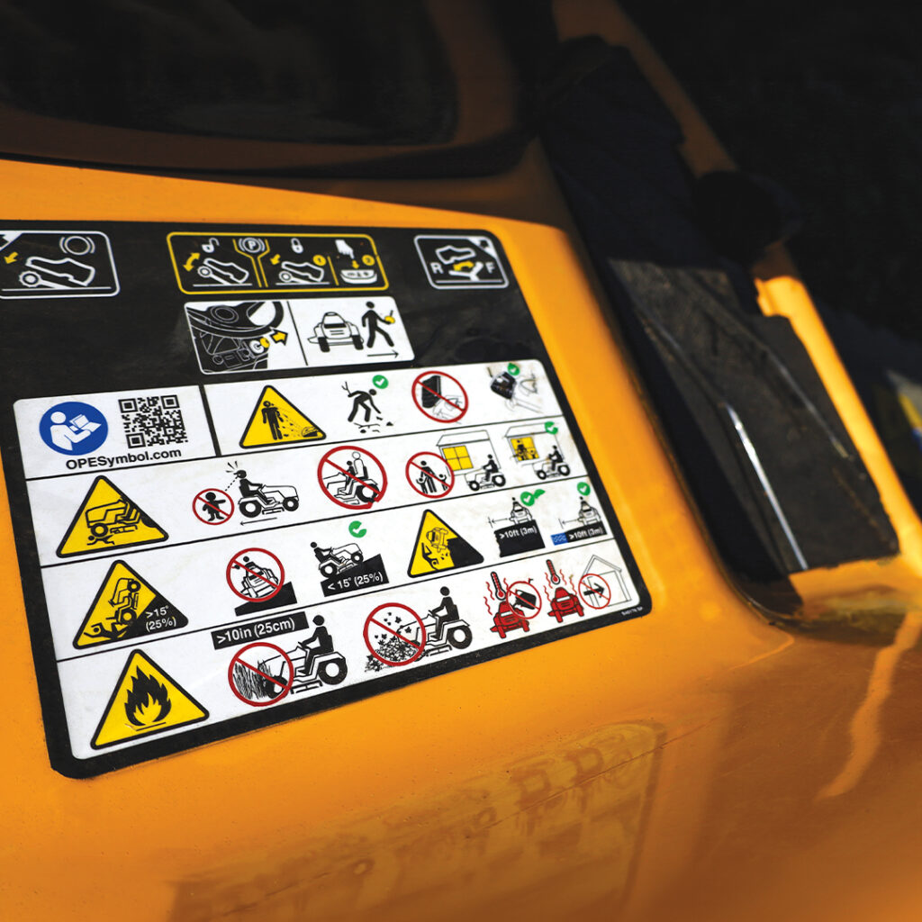Close-up of warning and safety instruction stickers with icons on a yellow industrial machine.