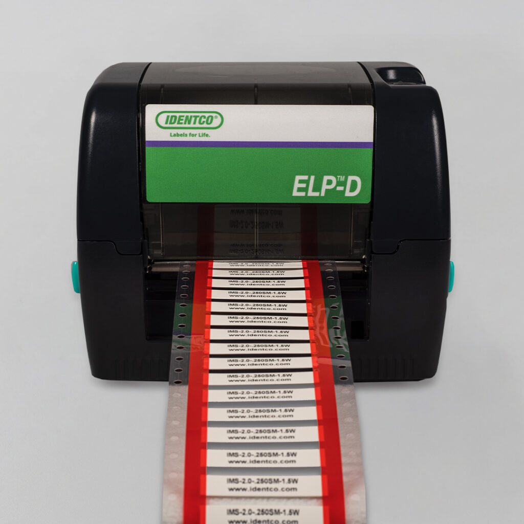Label printer with IDENTCO logo and ELP™D model prints white and red labels with black text, featuring green and purple panel.