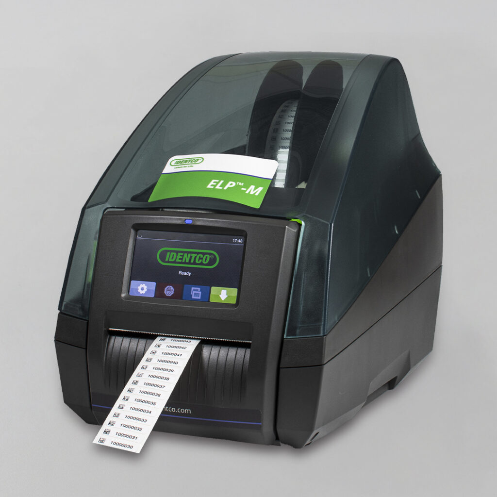 Black label printer with transparent cover prints barcode labels; green ELP-M card inserted on top; IDENTCO logo displayed on screen.