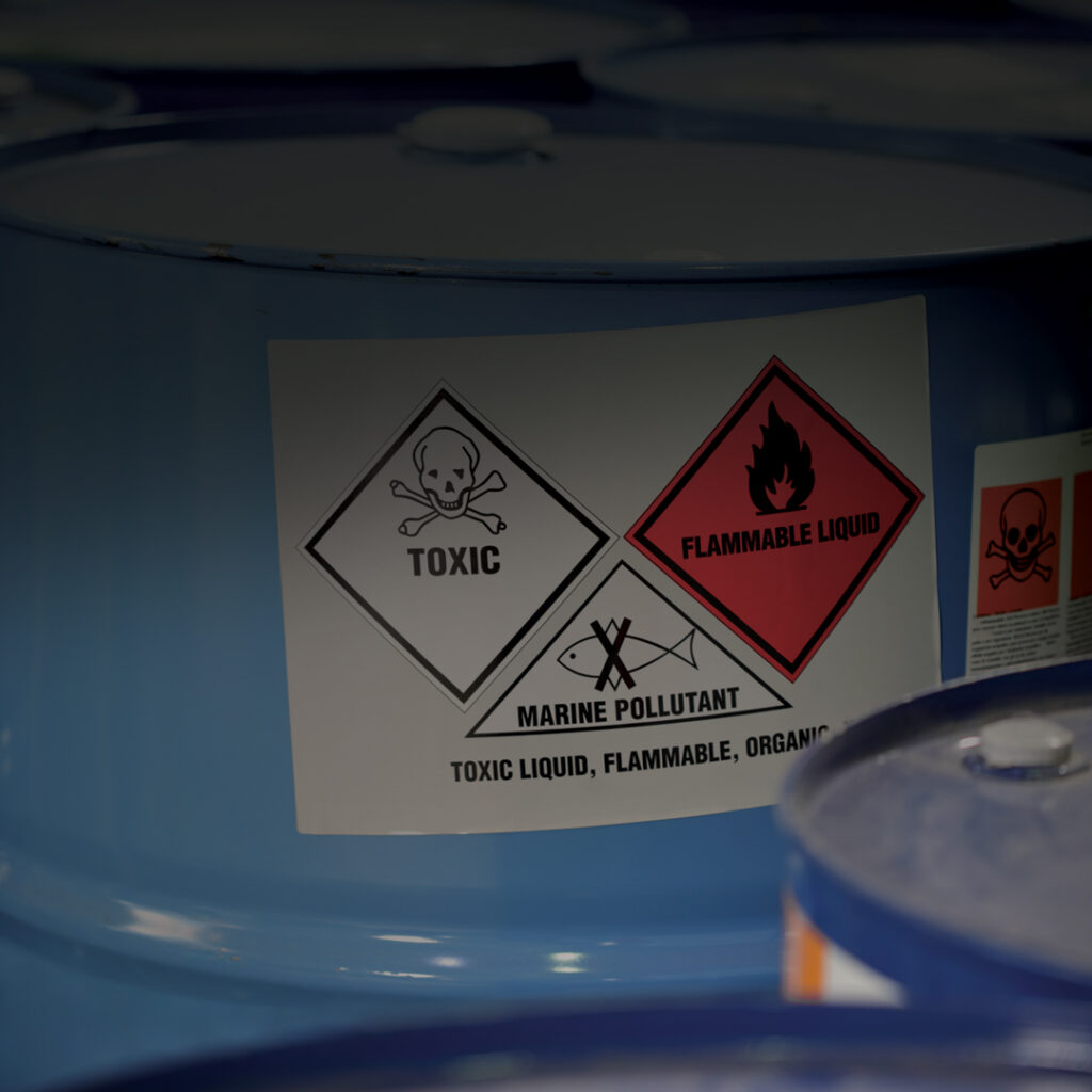 Blue barrels with labels displaying toxic, flammable liquid, and marine pollutant hazard symbols; warning text included.