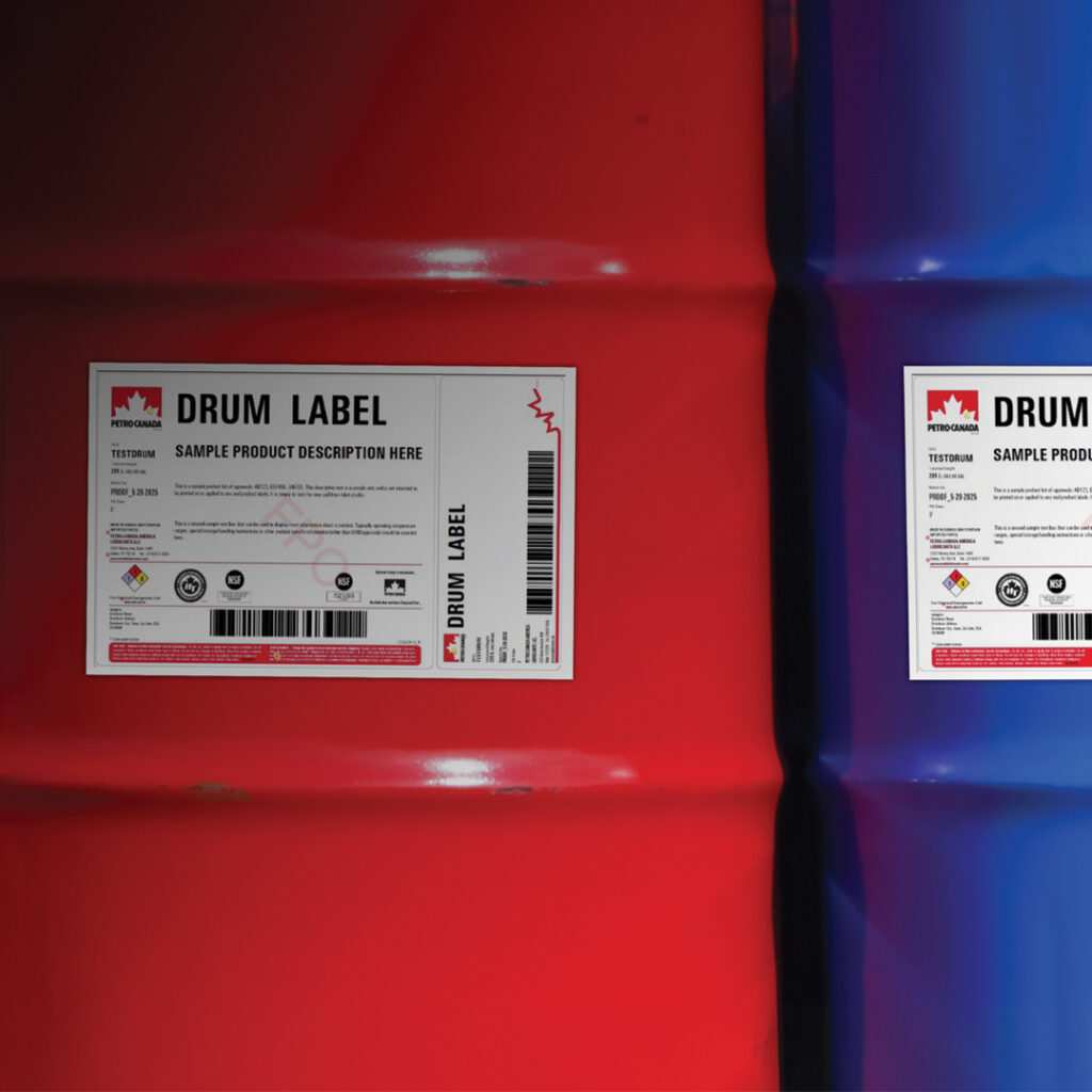 Red and blue Petro-Canada metal drums side by side, each with a white label, text, barcodes, and logo in the top left corner.