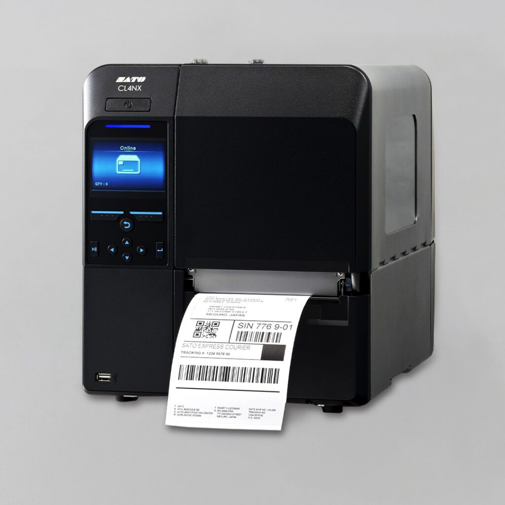 Black label printer with digital display prints shipping label with text and barcodes on white paper, set against a gray background.