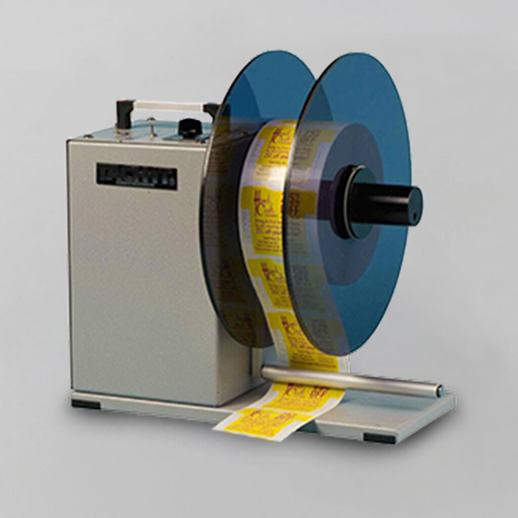 Label rewinder machine with blue spool winds yellow printed labels on gray surface against a plain light background.