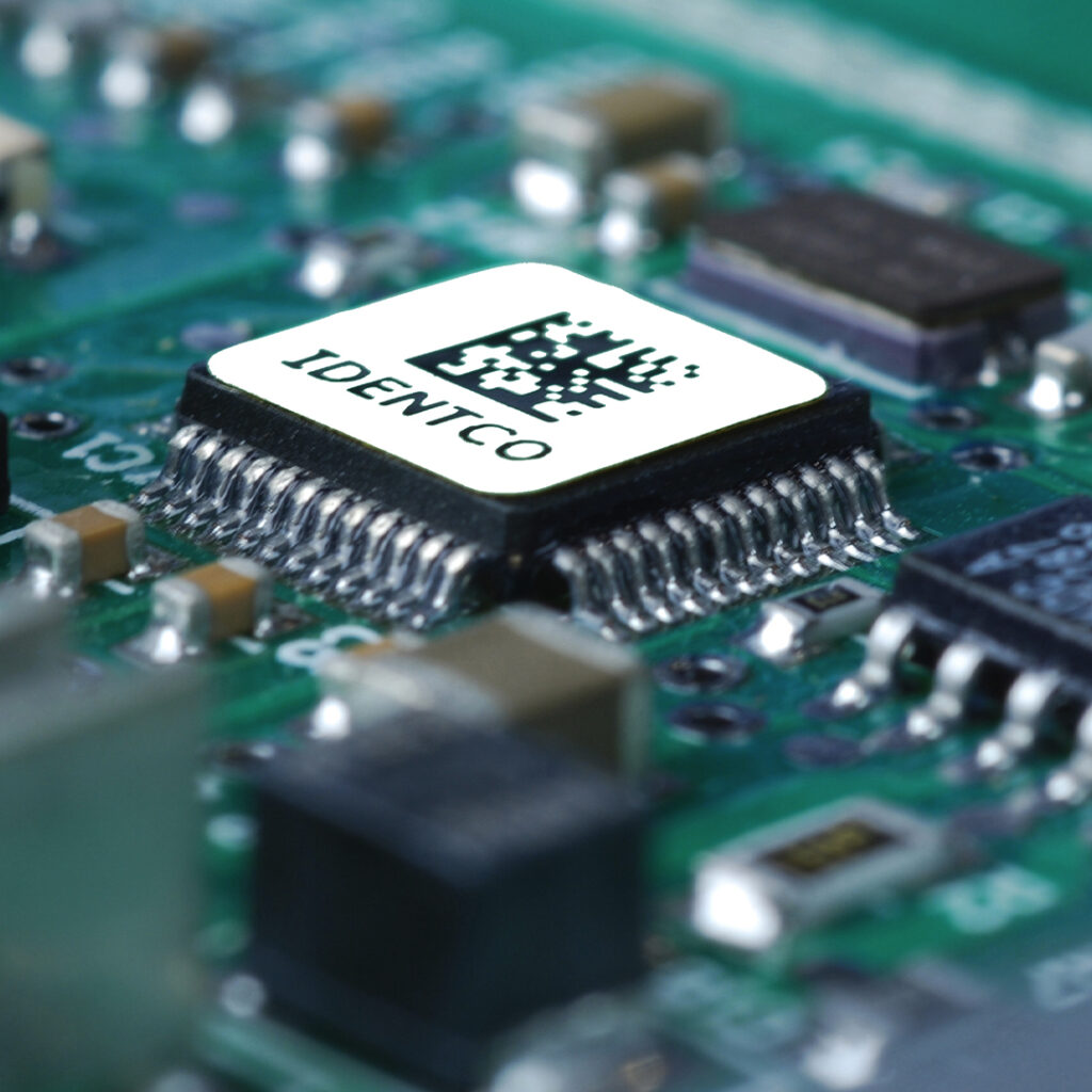 Close-up of a computer circuit board showing an IDENTCO microchip with QR code surrounded by components and detailed circuitry.
