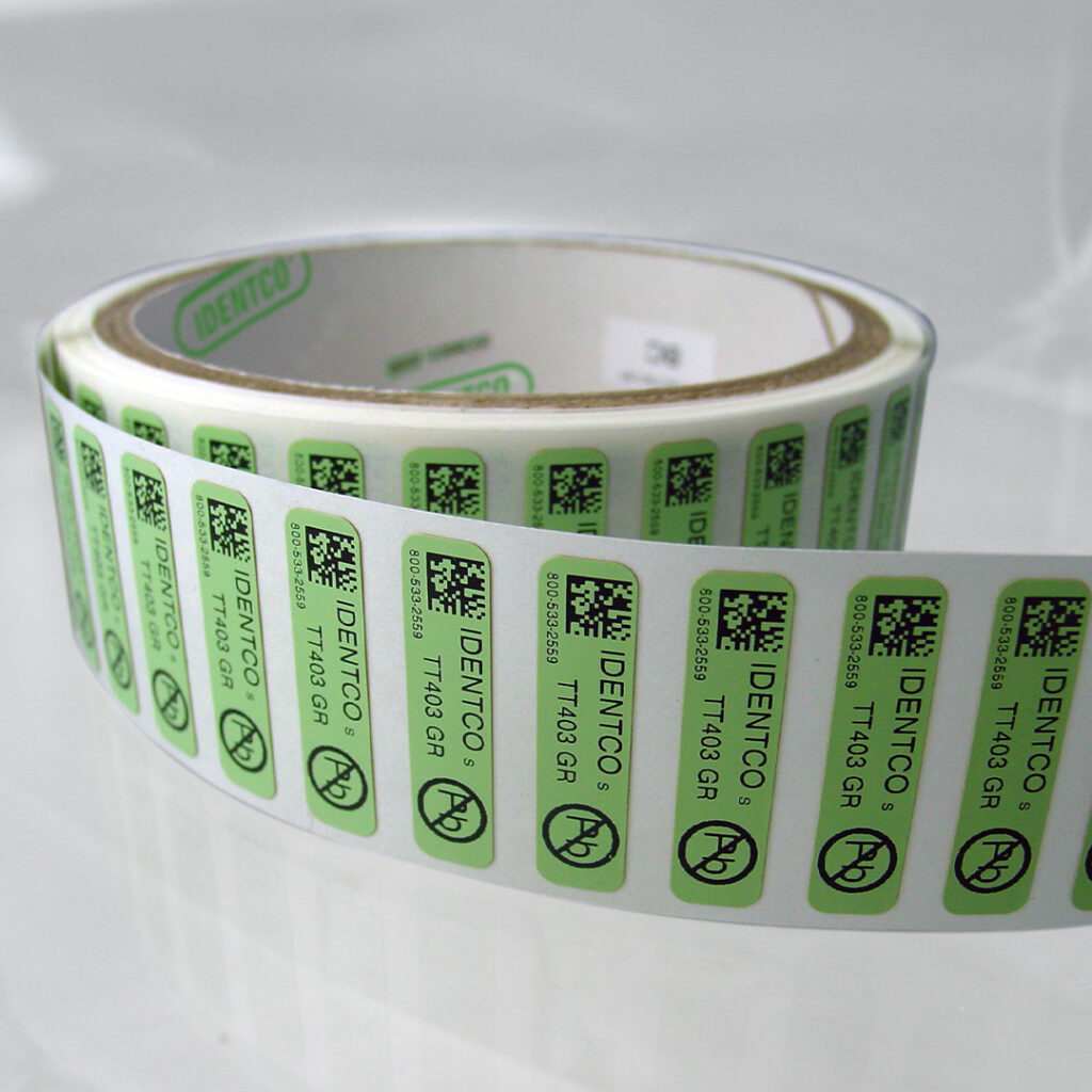 Green and white adhesive barcode labels with black text and symbols, partially unrolled on a glossy white surface.