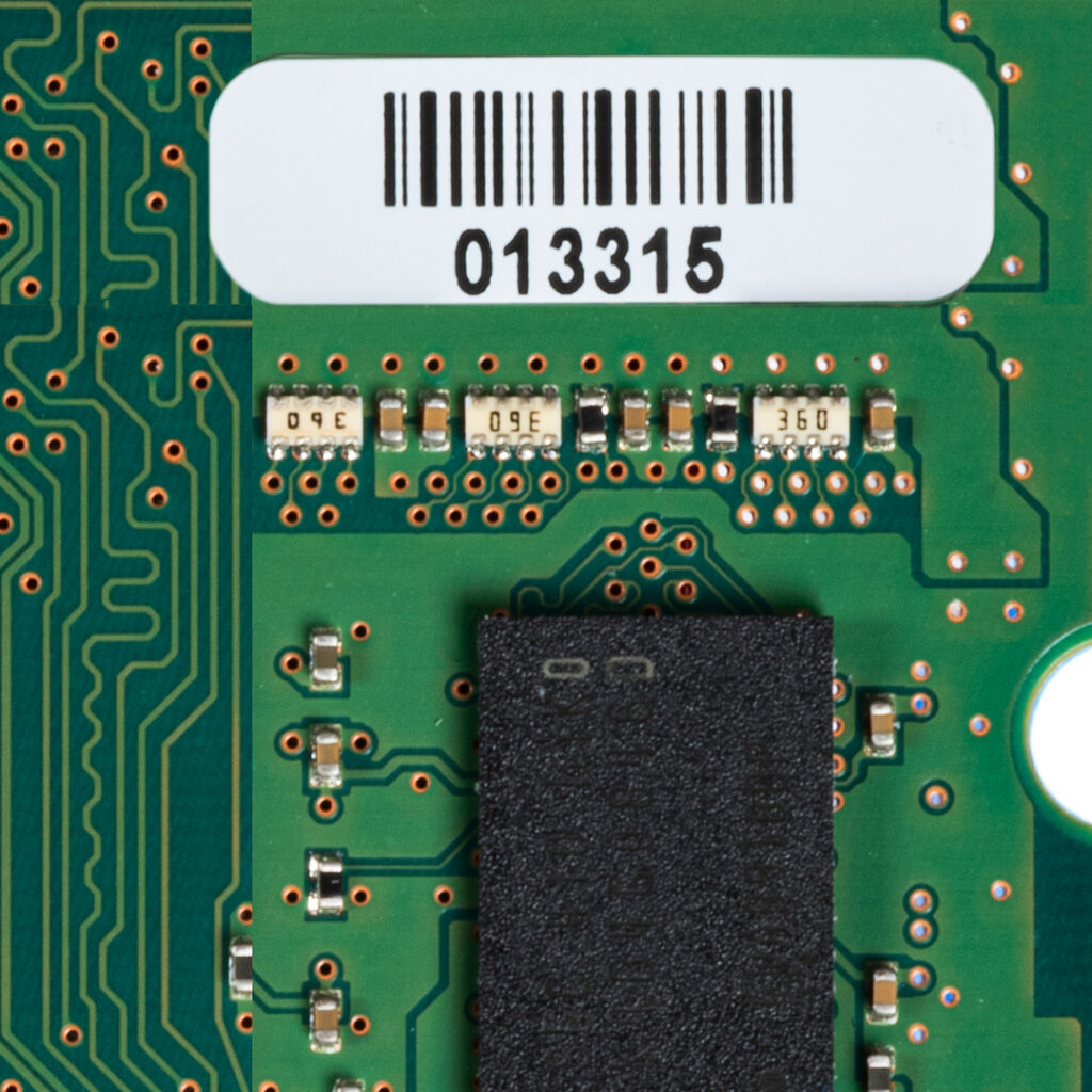 Close-up of green circuit board featuring microchips, resistors labeled 360, and a white barcode sticker showing number 013315 at the top.