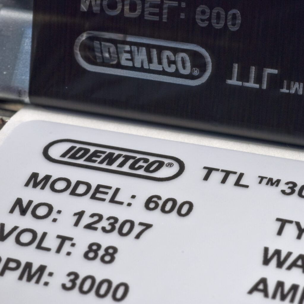 Close-up of IDENTCO label with model 600, serial 12307, voltage 88, RPM 3000, reflected on a shiny surface above.