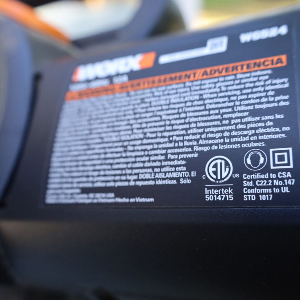 Warning label on WORX tool with safety info in English and Spanish, certification logos, and compliance details; text mostly blurred.