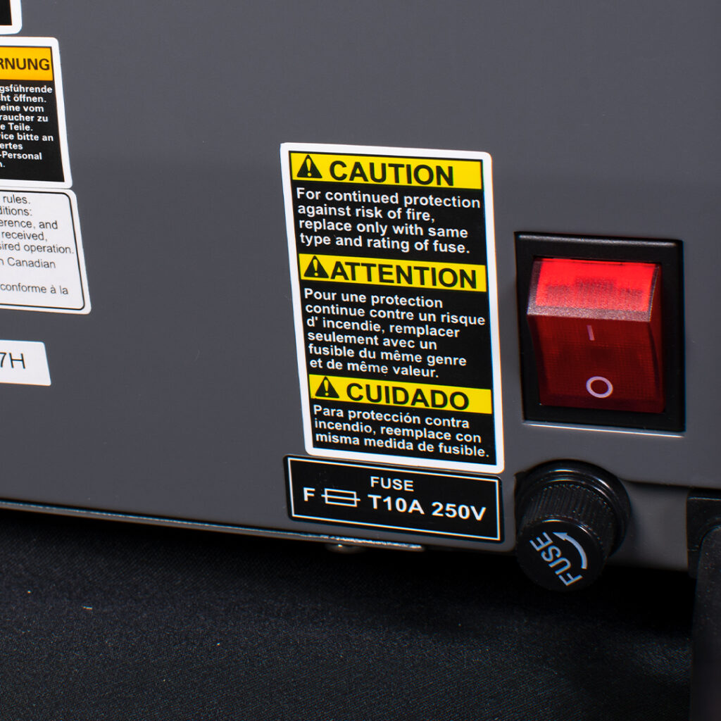 Close-up of electrical device with red power switch, multilingual caution labels, and fuse compartment labeled F T10A 250V on dark background.