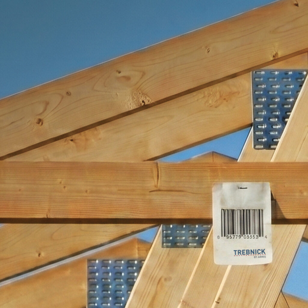 Wooden roof trusses with metal brackets under clear blue sky, beam labeled TREBNICK with visible barcode.