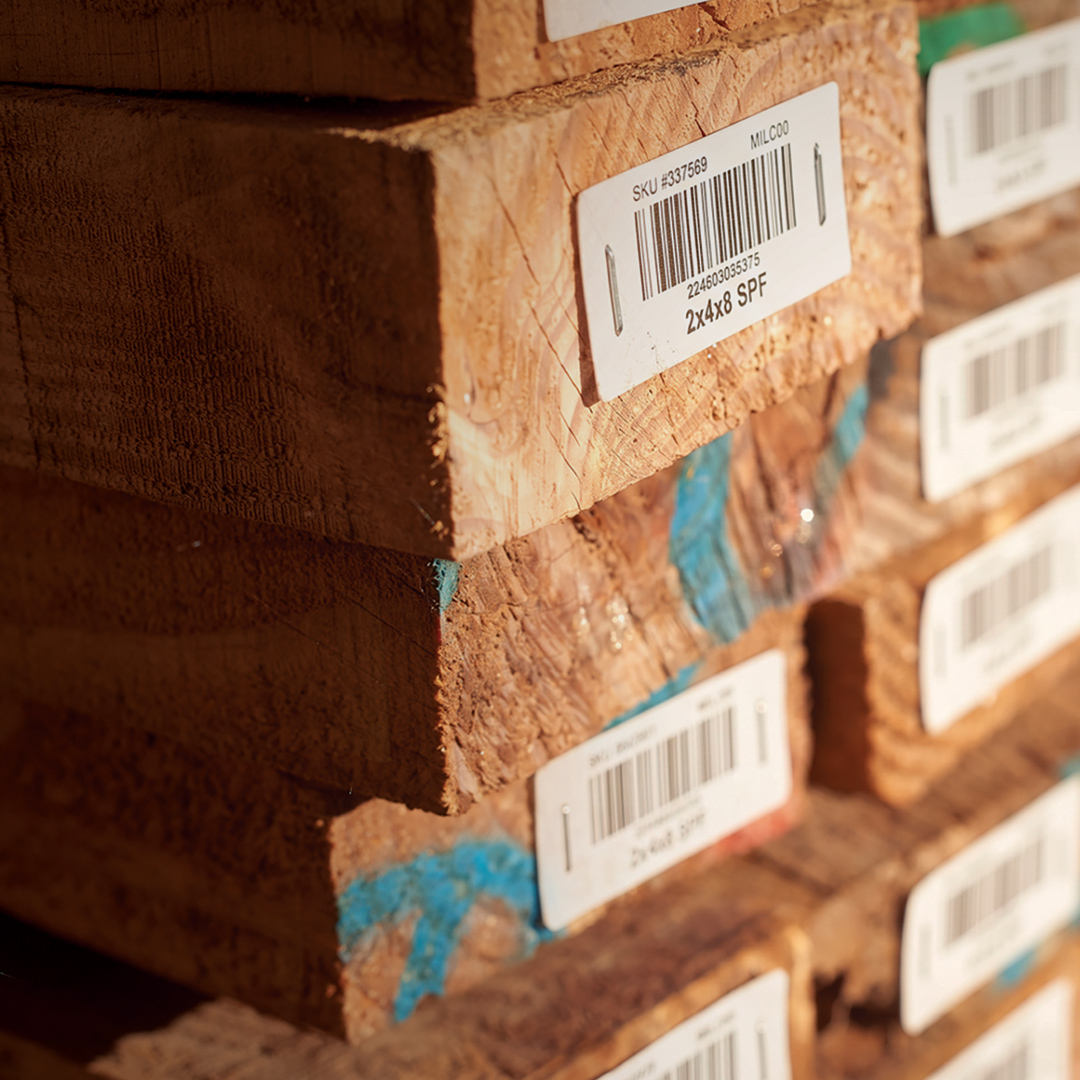 Stacked 2x4x8 SPF lumber with barcoded end labels, rough wood texture, and visible blue markings on some pieces.