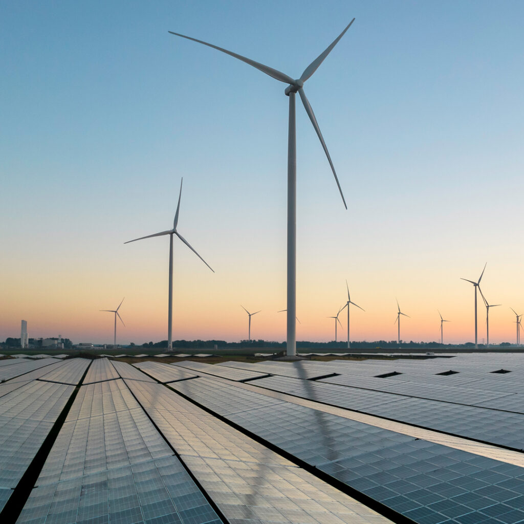 Wind turbines and a solar panel array generate renewable energy at sunset under a clear sky.