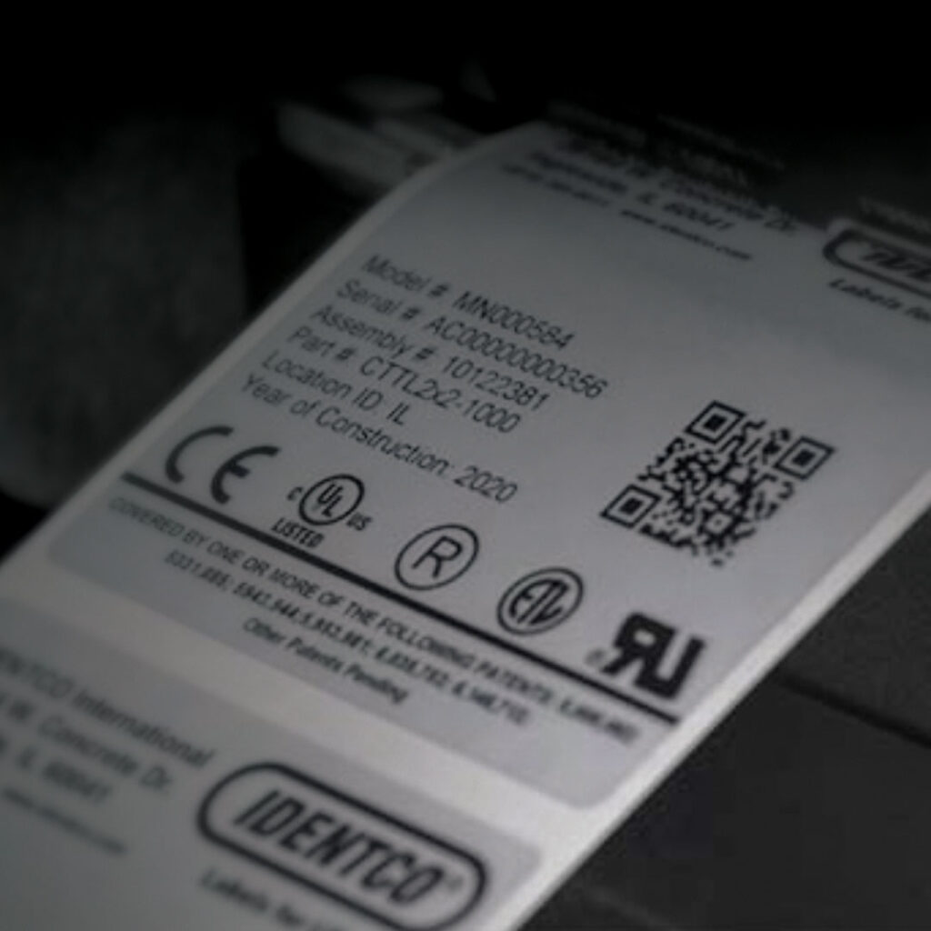 Close-up of a white product label with black text, QR code, barcodes, CE and UL marks, serial number, model number, and manufacturing info.