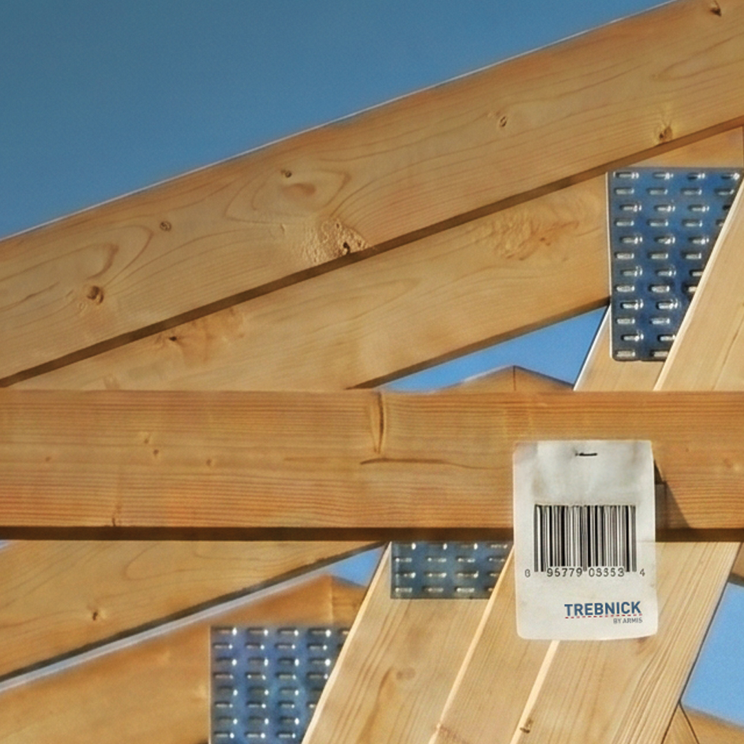 Wooden trusses with metal brackets under a blue sky, featuring a TREBNICK barcode sticker on one beam for material identification.