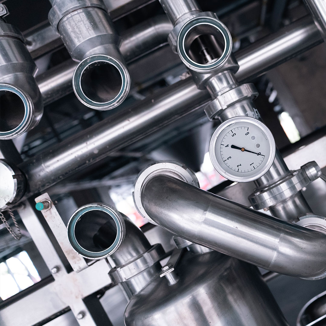 Close-up of industrial stainless steel pipes and fittings with a round analog pressure gauge attached, showing a complex network typically found in factories or processing plants.