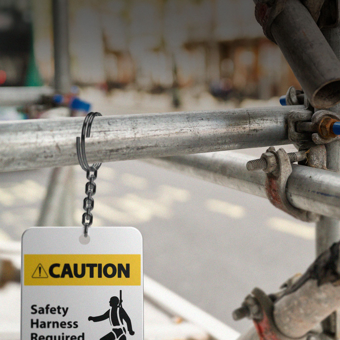 Caution sign on scaffolding requires safety harness, features harness illustration, bold yellow and black text; blurry construction site behind.