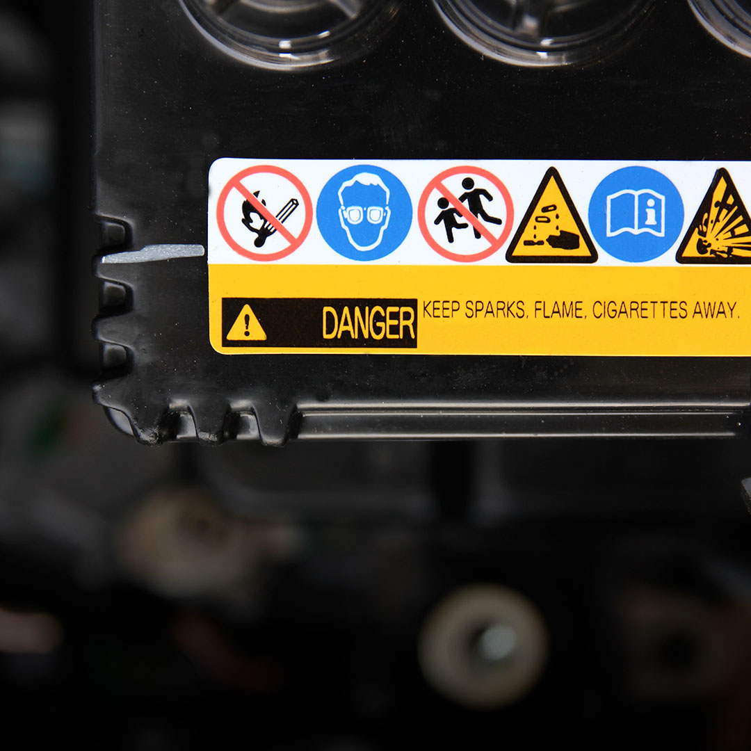 Warning label close-up: symbols for no flames, wear eye protection, no children, manual, explosion risk; text warns keep sparks away.