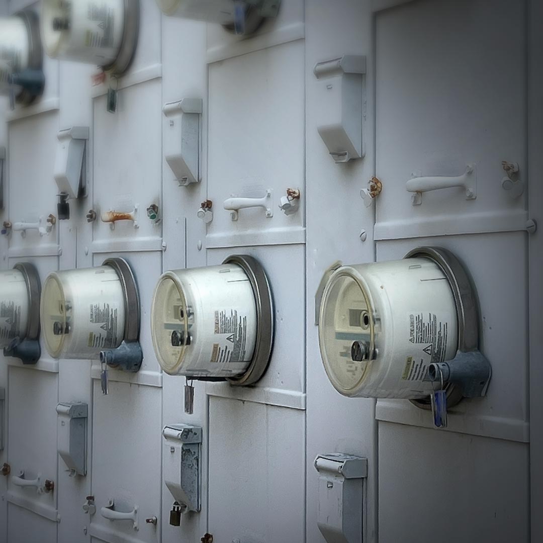 Row of electric meters with transparent covers and dials on a white utility panel, measuring household electricity consumption.