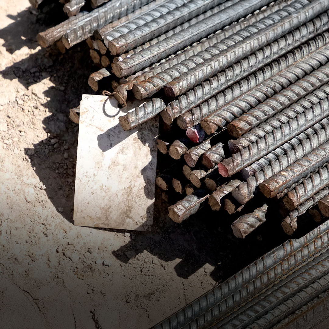 Steel rebar rods stacked on the ground at a construction site with a dirty white tag attached to one of the bundles.