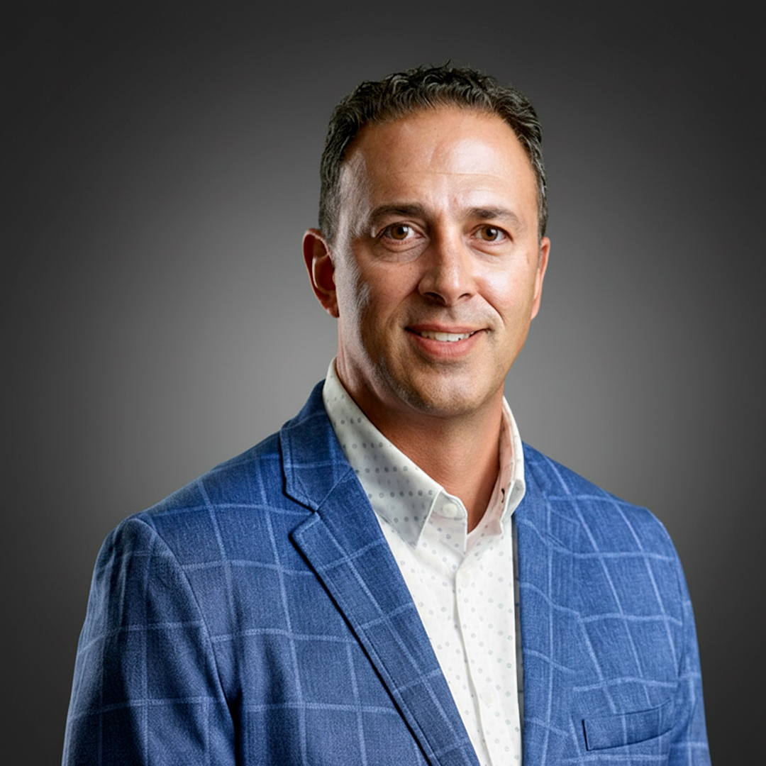 Man in light blue plaid suit jacket and white shirt smiles slightly against a dark gradient background.