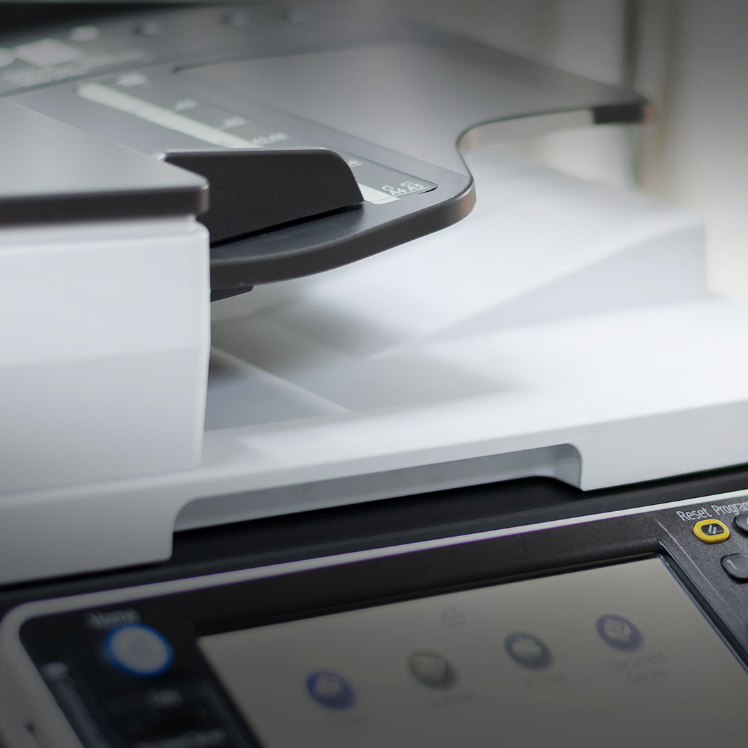 Modern office printer close-up showing paper tray, button control panel, and display screen, device powered on and ready for use.