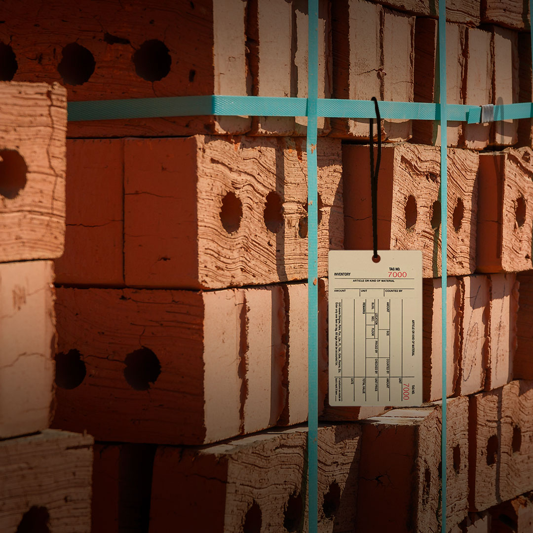 Red bricks with round holes stacked and secured by blue straps, a white tag with printed text and numbers attached in front.
