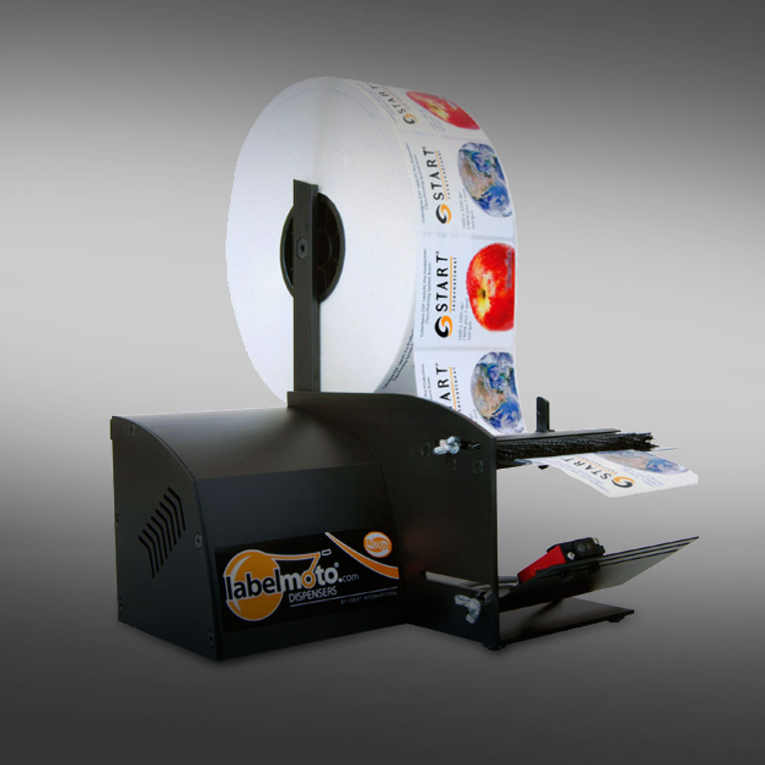 Label dispenser machine feeds colorful printed labels one at a time from a large roll, set on a gray gradient background.