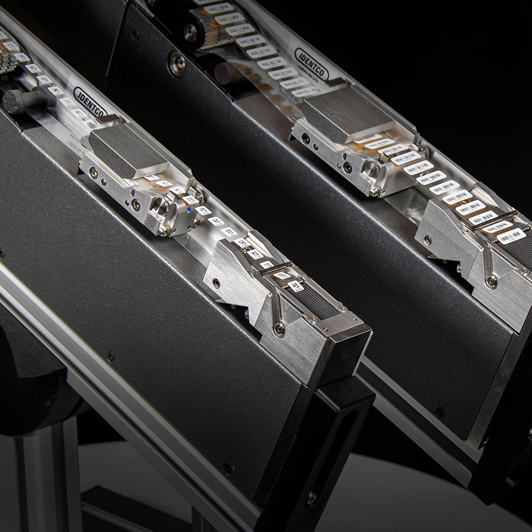 Close-up of two metallic industrial machines with labeled white plastic parts and moving components against a dark background.