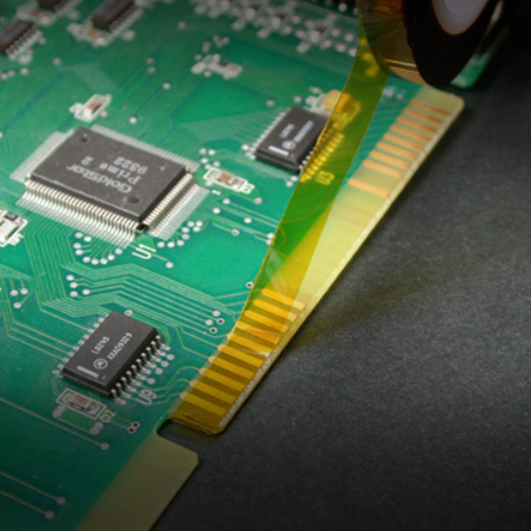 Close-up of a green circuit board featuring electronic components and yellow film partially covering gold connector pins along the edge.