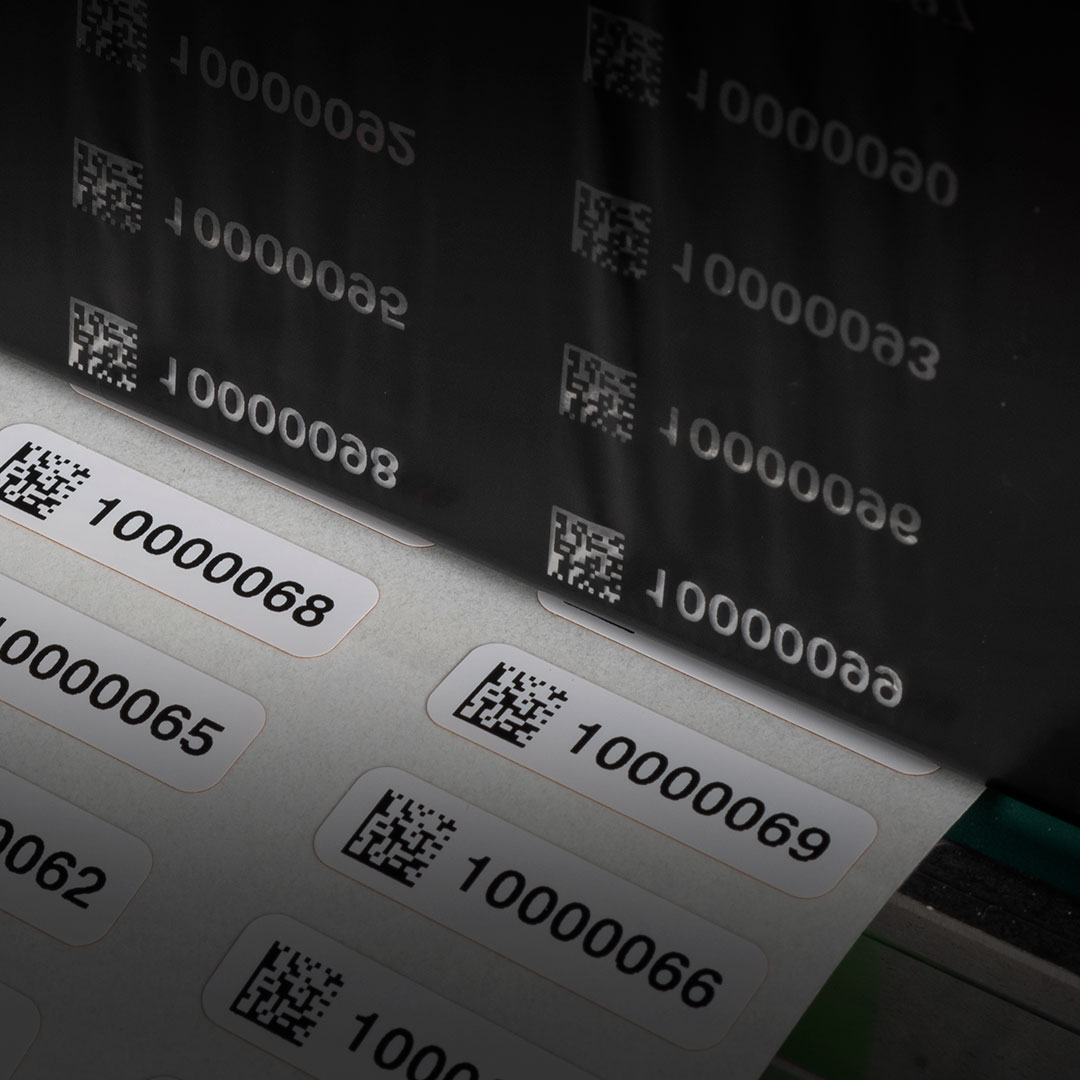 Sheet of white labels with black QR codes and serial numbers 10000068, 10000065, 10000062 printed; partial reflection above.