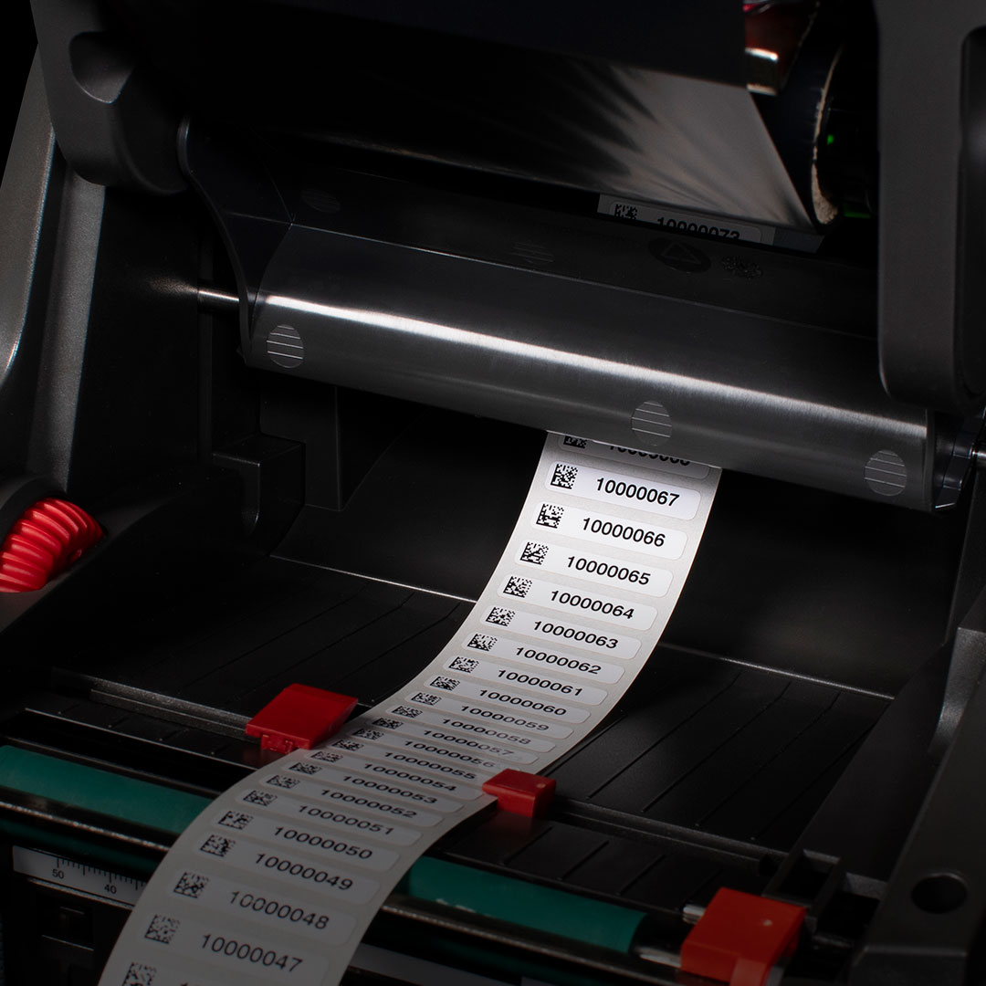 Label printer printing barcode labels with unique numbers, showing printer mechanism and machine interior for barcode production.