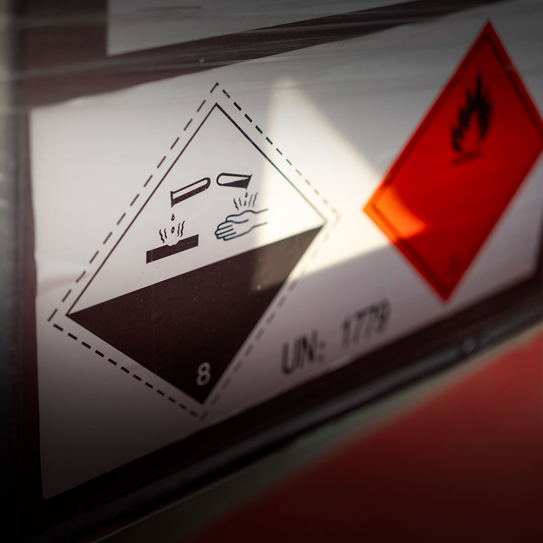 Close-up of a hazard label with a corrosive symbol showing liquid damaging a hand and surface, plus a partially visible flammable icon.
