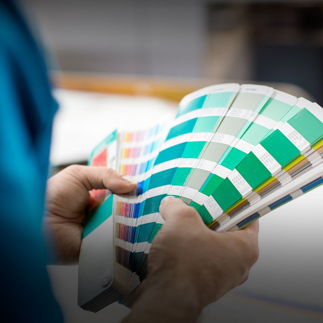 Person flipping through a color swatch book with green, blue, and other shades for design or printing selection.