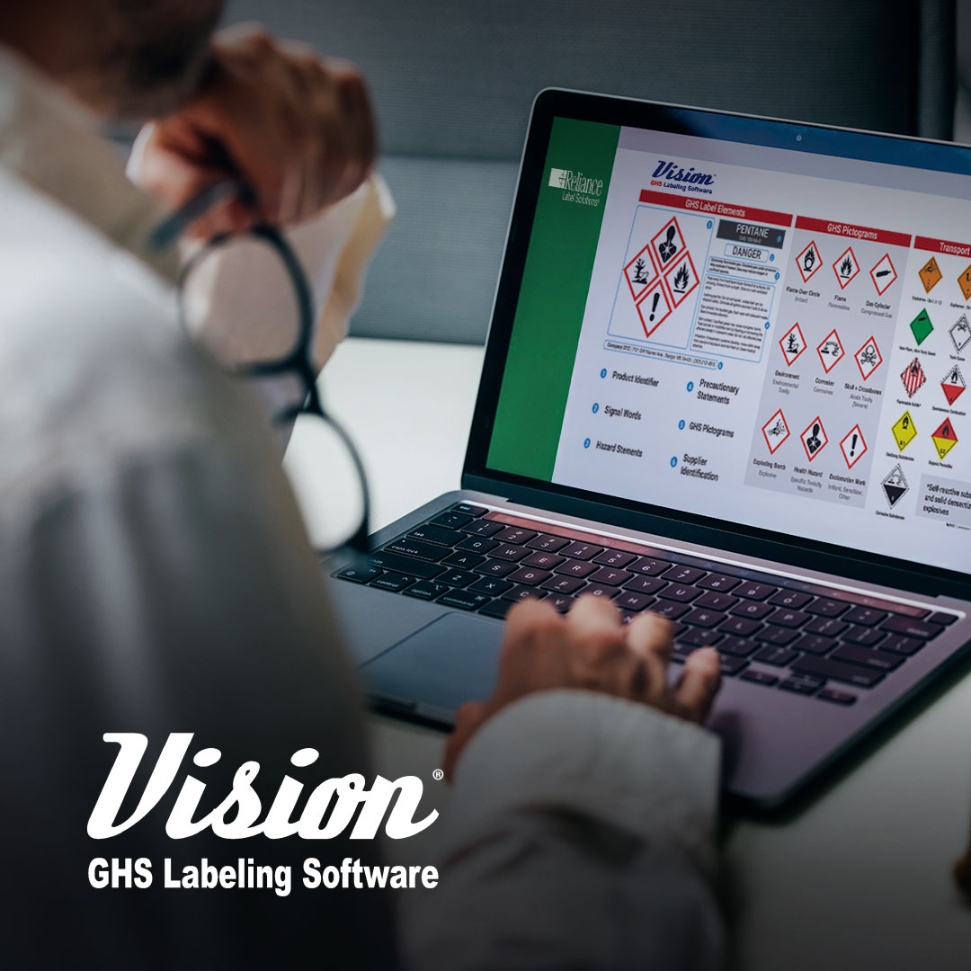 Person at desk with glasses uses laptop showing GHS hazard symbols, safety info, and Vision GHS Labeling Software text on screen.