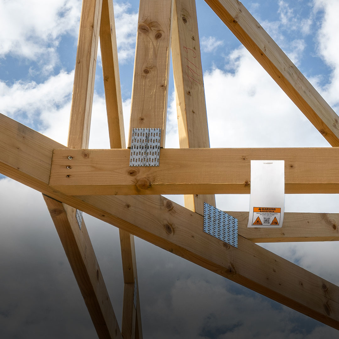 Wooden roof trusses with metal connector plates set against a partly cloudy sky at a construction site in progress.