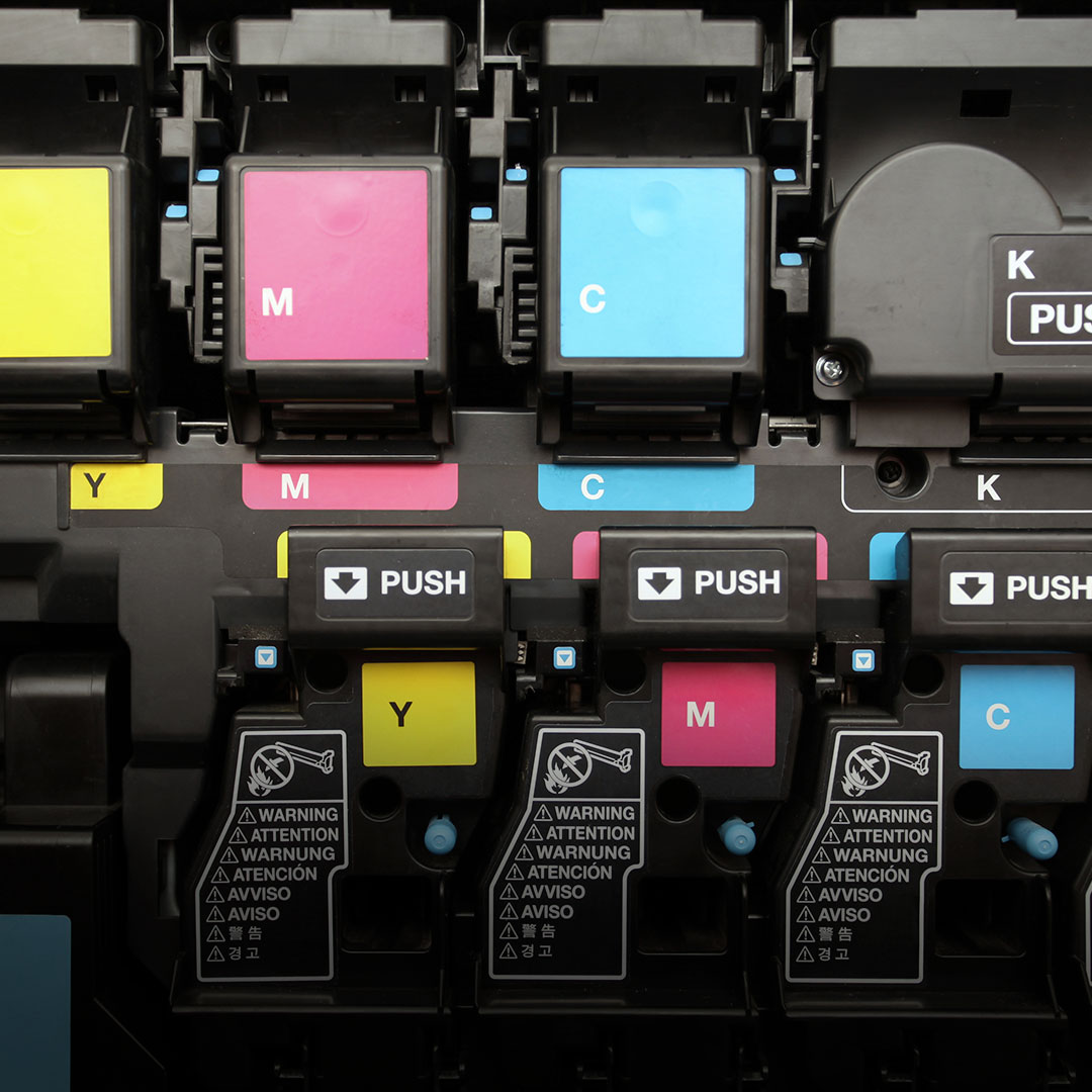 Close-up of yellow, magenta, cyan, and black printer ink cartridges with PUSH buttons and warning labels on each cartridge.