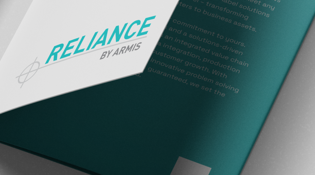 Close-up of a brochure titled RELIANCE BY ARMIS in bold teal and gray, partially open with blurred white text on a teal background inside.