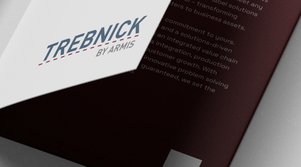 Close-up of a partially open brochure with TREBNICK BY ARMIS on the cover; blurred white text on a maroon background.