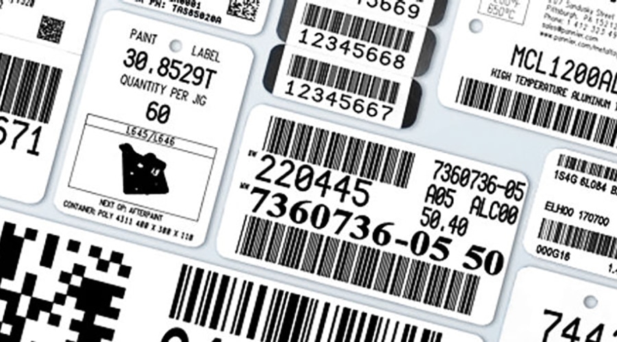 White adhesive labels with black barcodes, QR codes, alphanumeric codes, and manufacturing info scattered and overlapping.