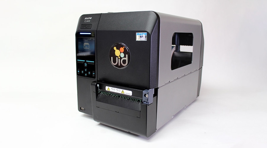 Black industrial label printer with uid logo, left-side screen and buttons, right label slot, on a plain white background.